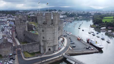 Ancient-Caernarfon-castle-Welsh-harbour-town-aerial-view-medieval-waterfront-landmark-right-orbit-to-stop