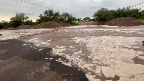 Foamy-brown-water-from-flash-flood-in-Arizona-rural-street,-panning