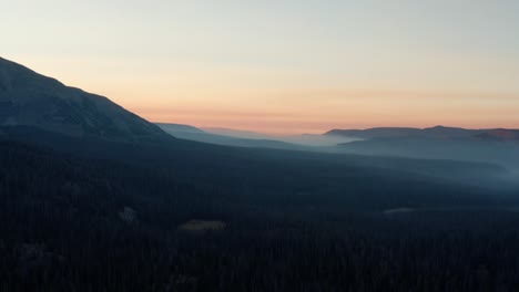 Beautiful-right-trucking-aerial-drone-shot-of-the-stunning-wild-Uinta-Wasatch-Cache-National-Forest-in-Utah-with-large-pine-trees-below-and-stunning-mountains-covered-in-mist-during-a-summer-sunrise
