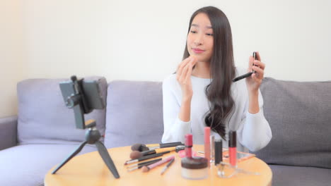 A-young-beautiful-woman-in-front-of-a-smartphone-in-video-mode-is-in-the-middle-of-a-social-media-makeup-tutorial