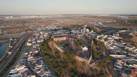Aerial-drone-flying-over-hilltop-Castelo-de-Castro-Marim-Castle,-village-settlements-and-salt-flats