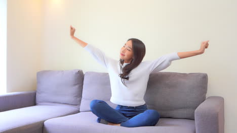 Junge-Asiatische-Frau,-Die-Ihre-Hand-Streckt,-Während-Sie-Auf-Der-Couch-In-Einem-Familienzimmer-Sitzt