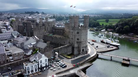 Ancient-Caernarfon-castle-Welsh-harbour-town-aerial-view-medieval-waterfront-landmark-slow-reverse-shot