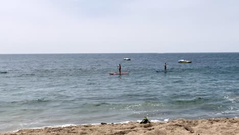 Two-male-paddle-boarders,-Malibu-beach-with-crashing-waves,-Pacific-Ocean