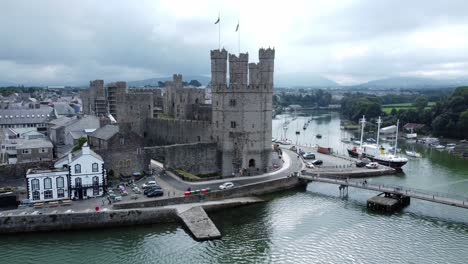 Ancient-Caernarfon-castle-Welsh-harbour-town-aerial-view-medieval-waterfront-landmark-orbit-right-above-river