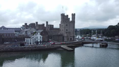 Ancient-Caernarfon-castle-Welsh-harbour-town-aerial-view-medieval-waterfront-landmark-low-angle-right-orbit
