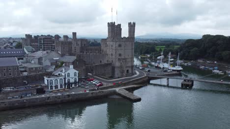 Ancient-Caernarfon-castle-Welsh-harbour-town-aerial-view-medieval-waterfront-landmark-slow-descend