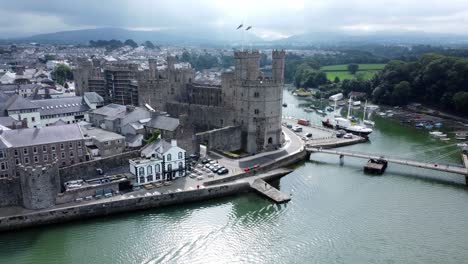 Ancient-Caernarfon-castle-Welsh-harbour-town-aerial-view-medieval-waterfront-landmark-pull-away-reveal