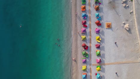 Schöner-Strand-Mit-Bunten-Sonnenschirmen-Auf-Sand,-Der-Von-Sauberem-Türkisfarbenem-Meerwasser-Im-Mittelmeer,-Albanien,-Gewaschen-Wird
