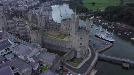 Ancient-Caernarfon-castle-Welsh-harbour-town-aerial-view-medieval-waterfront-landmark-high-up-left-dolly