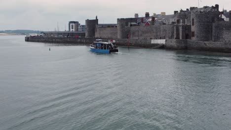 Following-sightseeing-boat-sailing-Caernarfon-castle-Welsh-harbour-town-river-aerial-view