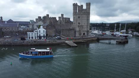 Sightseeing-boat-sailing-Caernarfon-castle-Welsh-harbour-town-river-aerial-view-tracking-left