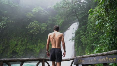 Man-walks-to-rail-overlooking-Rio-Celeste-waterfall-Costa-Rica,-slow-motion