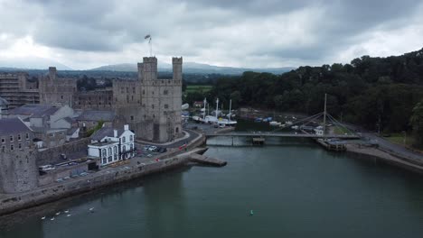 Ancient-Caernarfon-castle-Welsh-harbour-town-aerial-view-medieval-waterfront-landmark-slow-forward-shot