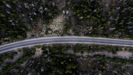Rotating-Aerial-top-bird's-eye-drone-shot-of-a-small-canyon-highway-in-the-Uinta-Wasatch-Cache-National-Forest-in-Utah-surrounded-by-large-pine-trees-on-a-gloomy-overcast-summer-day