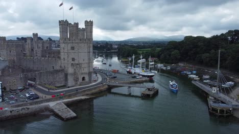 Ancient-Caernarfon-castle-Welsh-harbour-town-aerial-view-medieval-waterfront-landmark-right-orbit-slow-above-tourist-boat