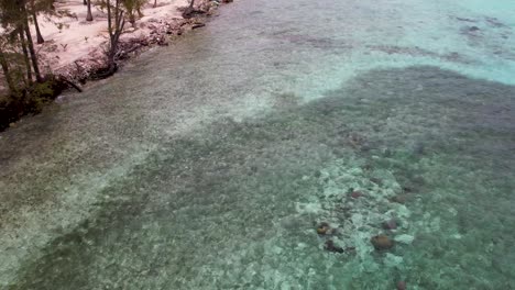 White-Sandy-beach-on-tropical-island-surrounded-by-coral-reef-and-crystal-clear-water,-aerial-view