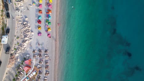 Ruhiger-Strand-Mit-Bunten-Sonnenschirmen,-Die-Von-Sauberem-Türkisfarbenem-Meerwasser-An-Der-Albanischen-Küste-Gewaschen-Werden