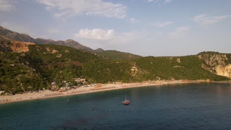 Idyllischer-Strand-An-Einem-Ruhigen-Ort,-Umgeben-Von-Grünen-Hügeln-Mit-Sonnenschirmen-Und-Ferienanlagen-In-Albanien