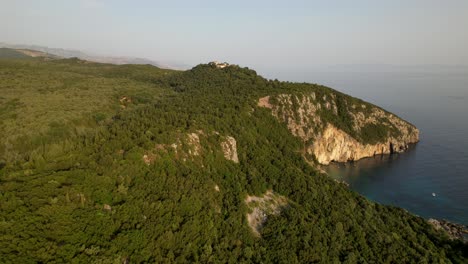 Beautiful-cape-covered-in-green-forest,-flying-over-old-monastery-with-sea-view-in-Mediterranean-coast