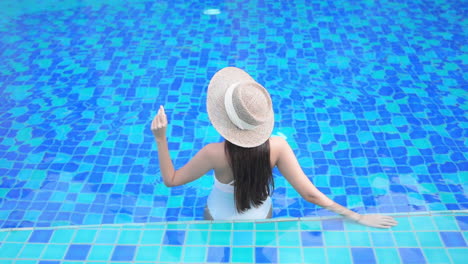 A-woman-with-her-back-to-the-camera-relaxes-in-a-blue-tiled-swimming-pool