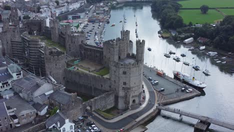 Ancient-Caernarfon-castle-Welsh-harbour-town-aerial-view-medieval-waterfront-landmark-quick-zoom-in