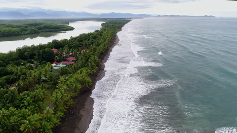 Wide-descending-aerial-of-palm-tree-lined-beach-with-reservoir-behind,-4K