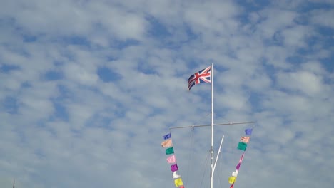 Pride-rainbow-flags-and-england-flag-at-the-top-with-partly-cloudy-sky-at-the-backround-slow-motion