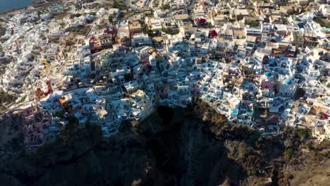 Top-down-aerial-spinning-over-famous-greek-village-Oia-with-white-cave-houses-and-villas-in-Santorini,-Greece