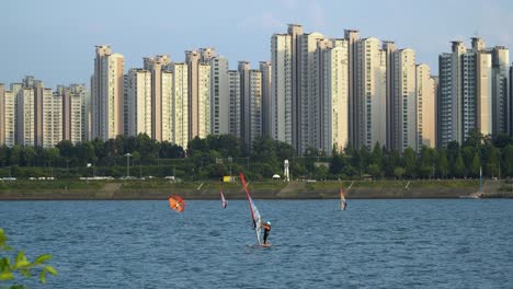 People-windsurfing-on-Han-river-at-sunset-on-complex-high-apartment-background,-Ttukseom-Surfing-club,-daytime-static