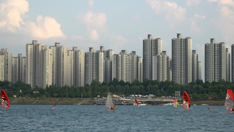 Two-windsurfers-rapidly-surfing-across-the-Han-river-at-sunset,-Jamsil-apartment-in-background,-beautiful-pinky-clouds-Seoul,-South-Korea