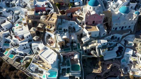 Close-aerial-top-down-view-of-Oia-with-white-cave-houses-and-villas-revealing-luxury-lifestyle-in-Santorini,-Greece