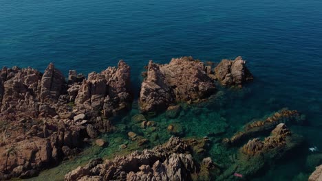 Aerial-of-a-scenic-natural-coast-beach-rock-bay-on-the-tourist-vacation-island-Sardinia-in-Italy-with-sun,-clear-blue-turquoise-and-calm-water-close-to-Capo-Testa