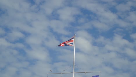 Britische-Flagge-An-Einem-Sonnigen-Tag-Mit-Wolken-Im-Höhepunkt-Gruppe-Von-Vögeln,-Die-Durch-Zeitlupe-Fliegen