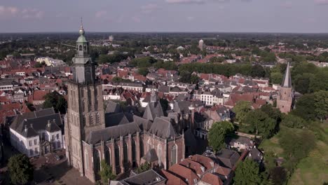 Rotating-aerial-around-Walburgiskerk-cathedral-with-golden-weathercock-in-medieval-Hanseatic-town-Zutphen-in-The-Netherlands-showing-Drogenapstoren-and-watertower-in-the-back-in-flat-Dutch-landscape