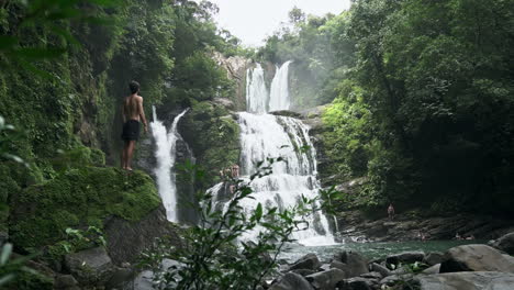Wide-shot-of-man-in-front-of-Nauyaca-waterfalls-Costa-Rica-jungle,-slow-motion