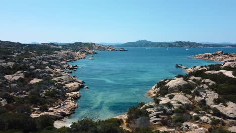 Aerial-of-an-idyllic-natural-coast-beach-rock-bay-at-La-Maddalena-on-the-tourist-vacation-island-Sardinia-in-Italy-with-sun,-clear-blue-turquoise-and-calm-water