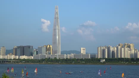 People-doing-water-sports-on-Han-river---windsurfing,-kayaking,-paddleboarding,-riding-a-canoe,-water-ski---Lotter-World-Tower-on-Background-on-a-beautiful-sunny-day,-Jamsil,Seoul,-South-Korea