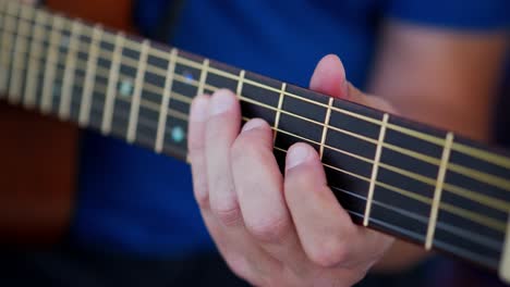 Fingers-of-Caucasian-white-man-wearing-blue-shirt-playing-an-acoustic-guitar-close-up-at-top-of-fret-board