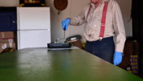 Cropped-Image-Of-A-Man-Coating-Wooden-Table-Surface-With-Green-Paint-Using-Roller-Brush-At-The-Garage