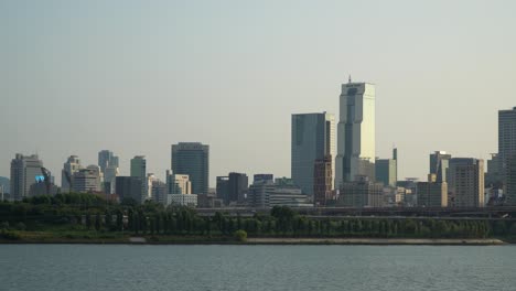Torre-Comercial-Coreana-Y-Muchos-Rascacielos-Y-Edificios-Altos-A-La-Luz-Del-Atardecer-Desde-El-Paseo-Marítimo-Del-Río-Han,-Tráfico-De-Automóviles-En