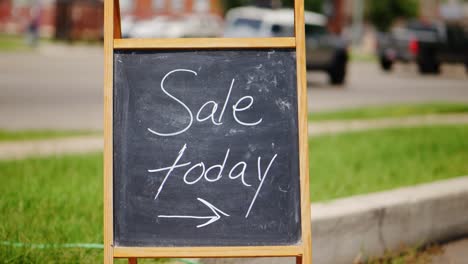 Sale-today-chalkboard-and-wood-A-frame-sign-outside-next-to-green-grass-and-road-with-cars-driving-by-in-the-middle-of-the-day,-centered-in-frame