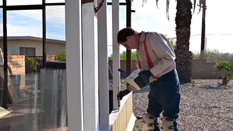 Homeowner-Brushing-White-Paint-On-Wooden-Patio-During-House-Construction