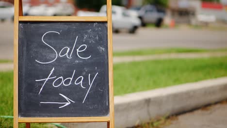 Sale-today-chalkboard-and-wood-A-frame-sign-outside-next-to-green-grass-and-road-with-cars-driving-by-in-the-middle-of-the-day,-panning-side-to-side