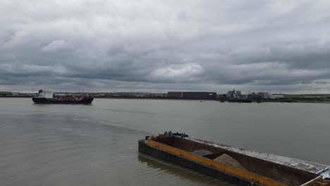 Drone-footage-Large-ship-moving-along-River-Thames-near-Rainham-Essex-UK-Barge-in-foreground