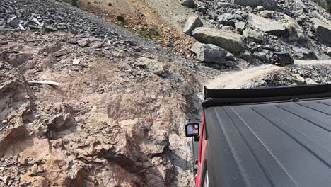Rooftop-of-4WD-vehicle-following-another-on-rocky-narrow-trail-cut-in-mountain-side-with-sheer-drop-off