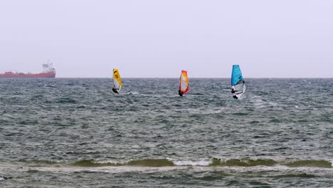 Orange-and-Blue-windsurfing-Riding-the-Waves-in-a-Choppy-Sea-and-Big-Boat-on-Background