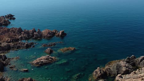 Aerial-of-an-idyllic-natural-coast-beach-rock-bay-on-the-tourist-vacation-island-Sardinia-in-Italy-with-sun,-clear-blue-turquoise-and-calm-water-close-to-Capo-Testa
