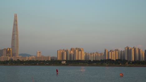 Lotter-tower-and-people-windsurfing-and-surfing-with-echo-wing-at-sunset,-Jamsil-apartment-urban-background,-Seoul-city-skyline
