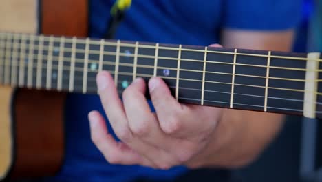 Fingers-of-Caucasian-white-man-with-blue-shirt-playing-an-acoustic-guitar-close-up-moving-from-the-top-of-fret-board-to-bottom-playing-a-solo-riff